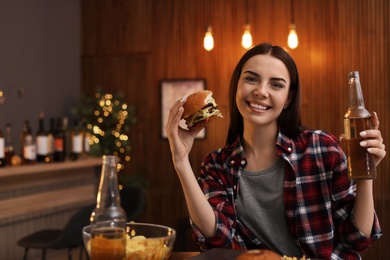 Photo of Young woman with beer eating tasty burger in cafe