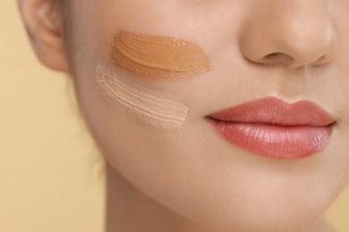 Woman with swatches of foundation on face against beige background, closeup
