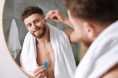 Photo of Handsome man applying serum onto his face near mirror in bathroom