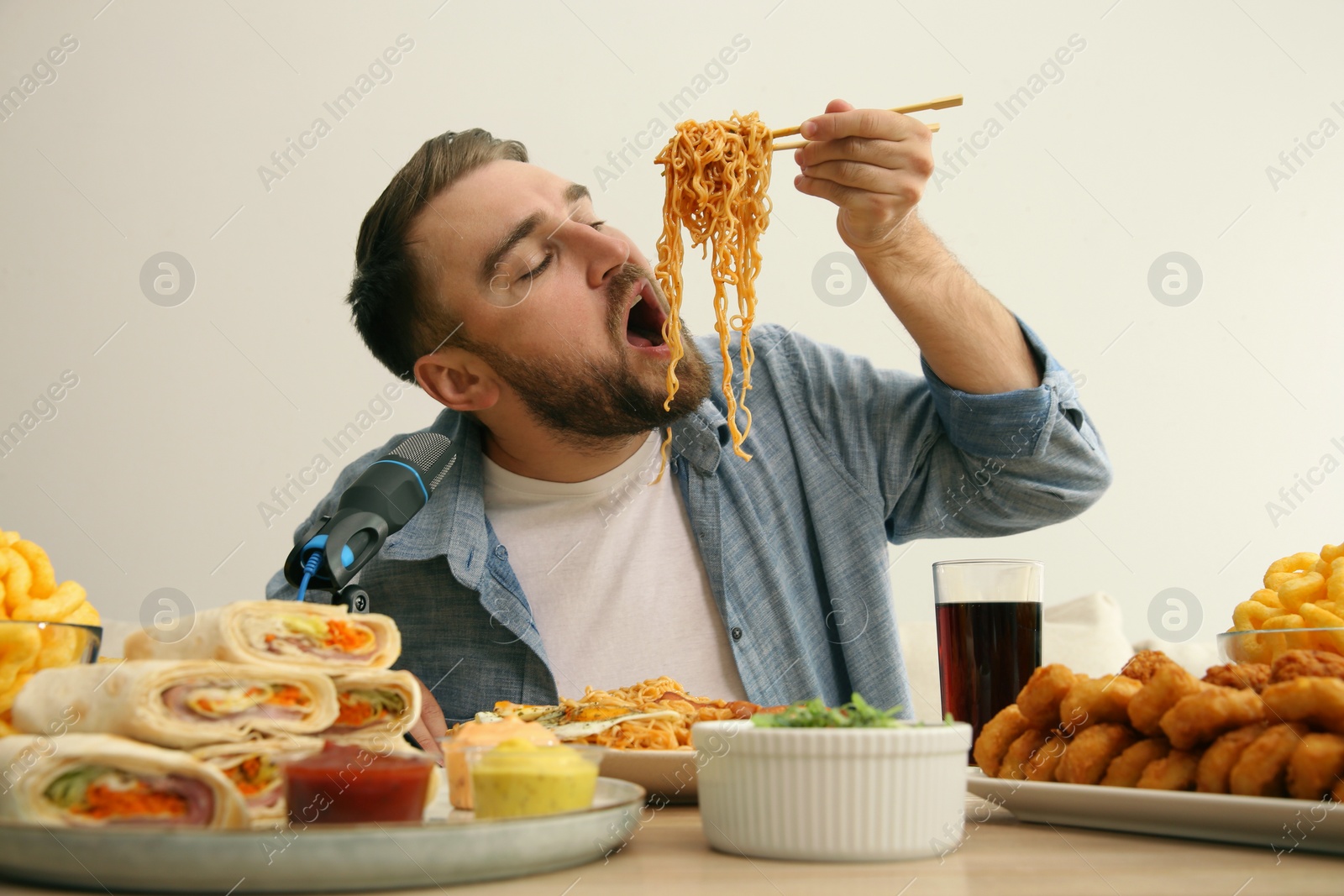 Photo of Food blogger eating in front of microphone at table against light background. Mukbang vlog