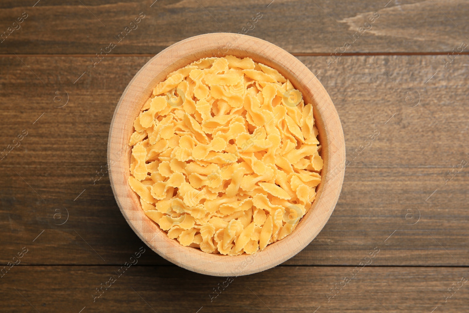 Photo of Raw farfalline pasta in bowl on wooden table, top view