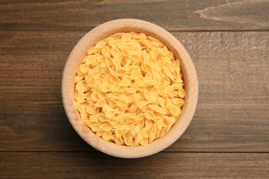 Raw farfalline pasta in bowl on wooden table, top view