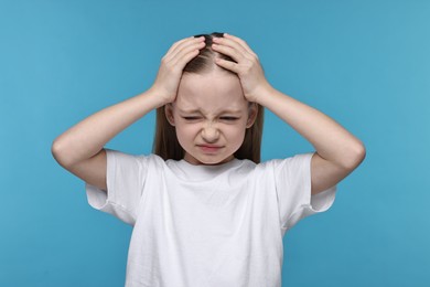 Photo of Little girl suffering from headache on light blue background