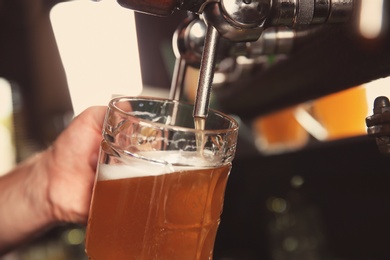 Bartender pouring beer from tap into glass in bar, closeup