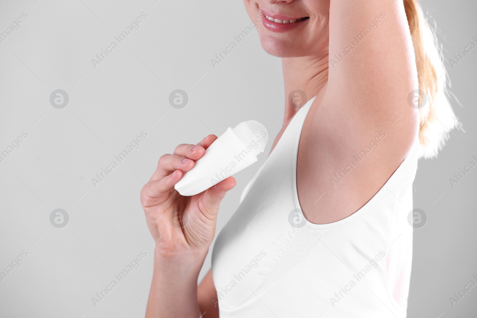 Photo of Young woman using deodorant on grey background, closeup. Space for text