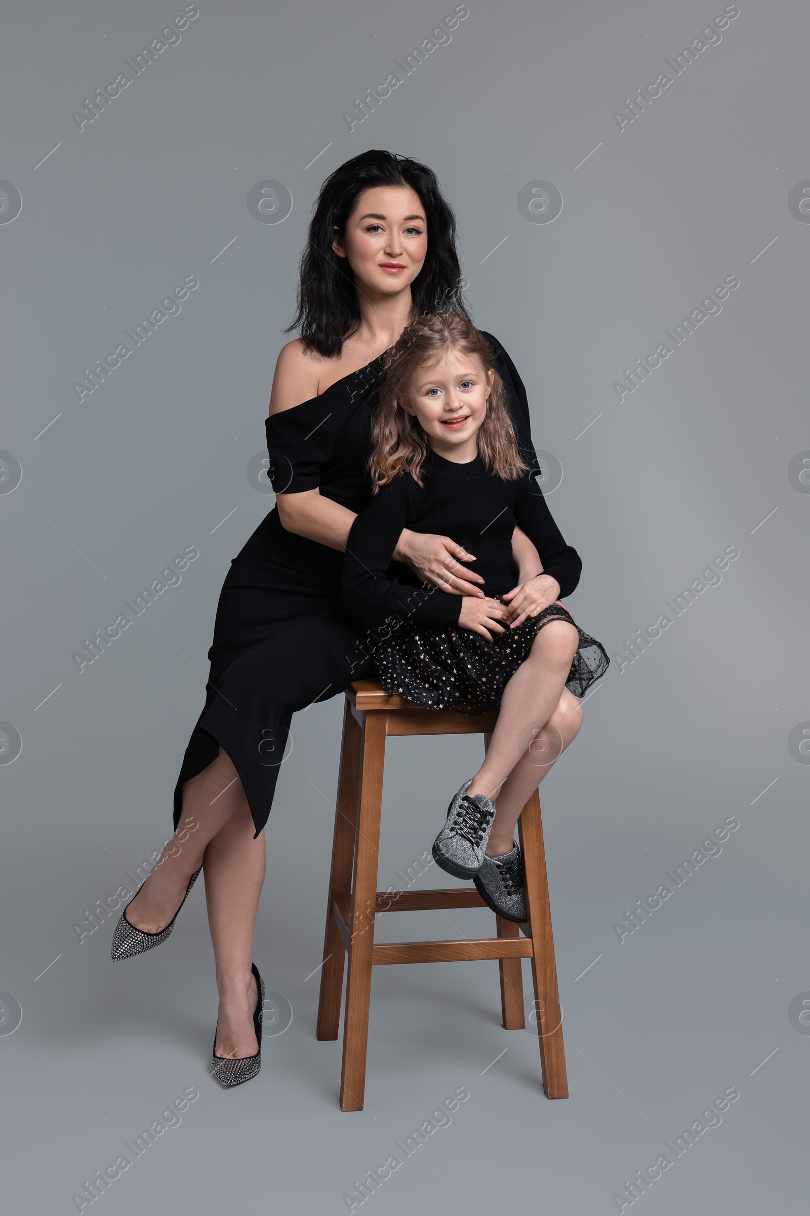 Photo of Beautiful mother with little daughter on stool against grey background