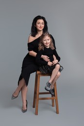 Beautiful mother with little daughter on stool against grey background