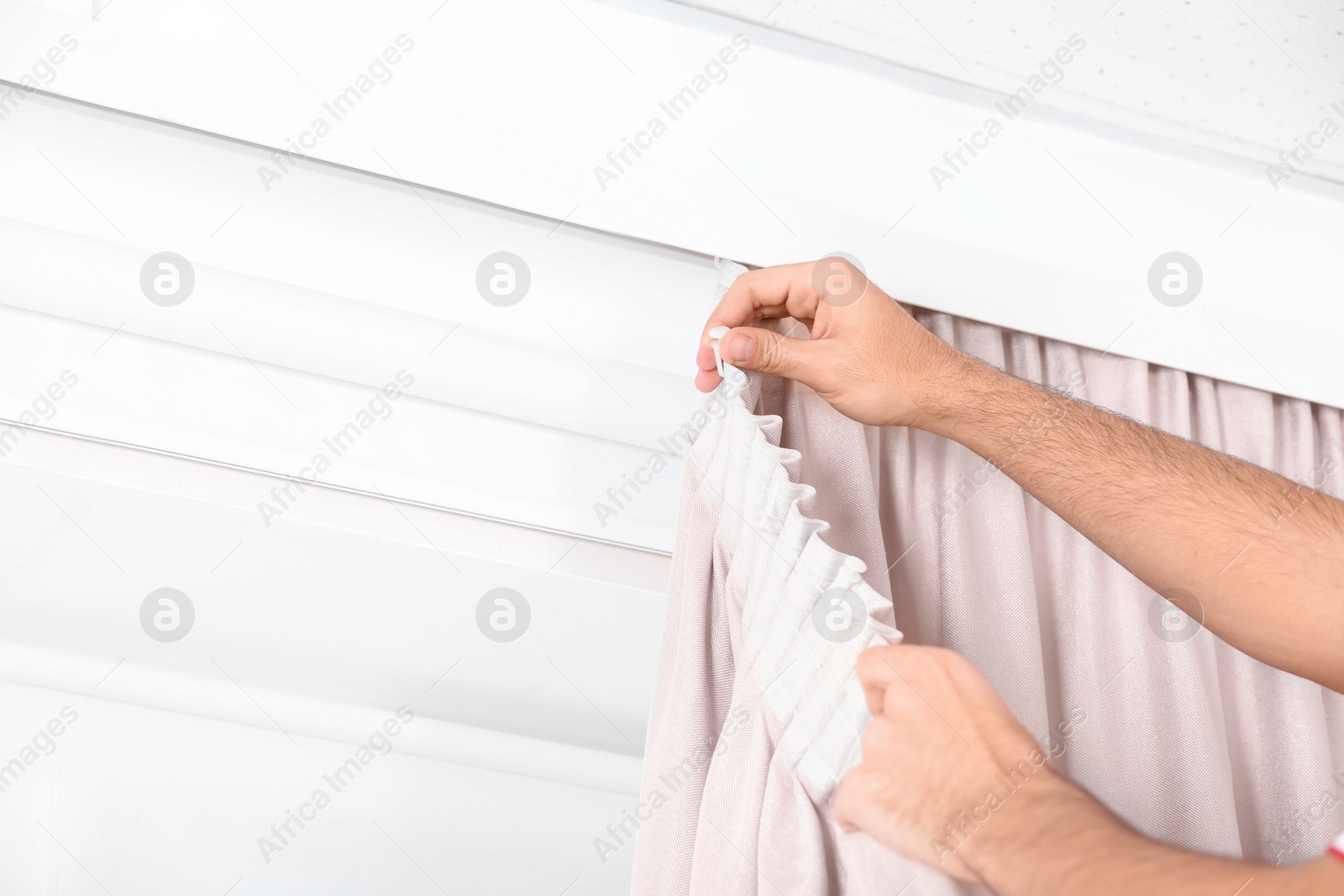 Photo of Young man hanging window curtain in room, closeup. Space for text