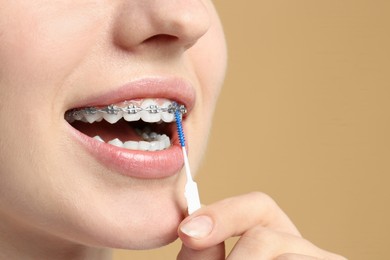 Photo of Woman with dental braces cleaning teeth using interdental brush on beige background, closeup. Space for text