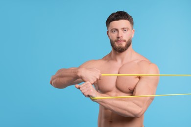 Photo of Young man exercising with elastic resistance band on light blue background. Space for text