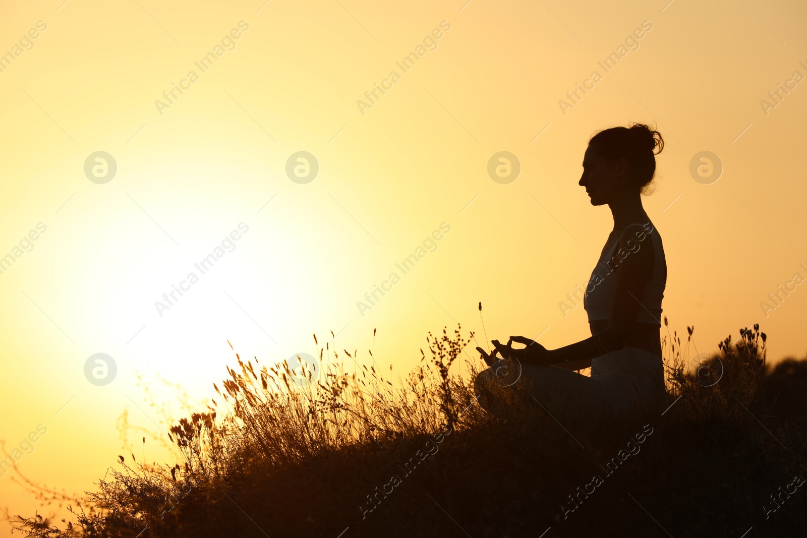 Photo of Silhouette of woman meditating outdoors at sunset. Space for text