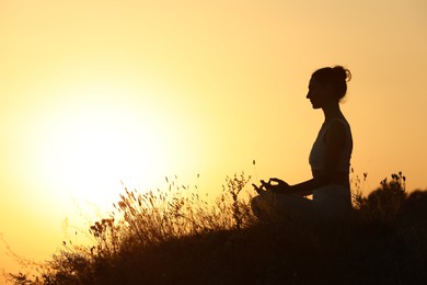 Photo of Silhouettewoman meditating outdoors at sunset. Space for text