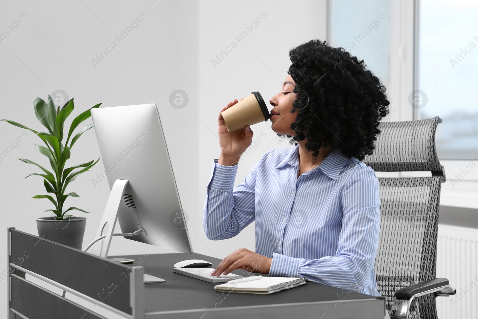 Photo of Young woman drinking coffee while working on computer in office