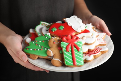 Woman with plate of delicious gingerbread Christmas cookies on black background, closeup