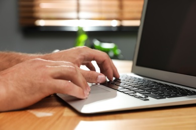 Photo of Man using laptop for search at wooden table indoors, closeup