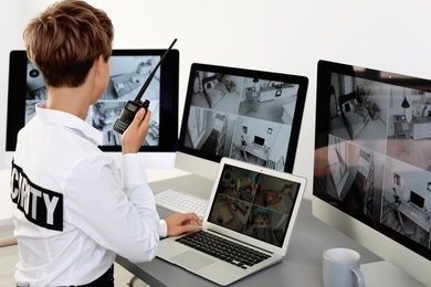 Female security guard with portable transmitter monitoring home cameras indoors