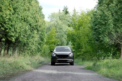 Photo of New black modern car on road near trees