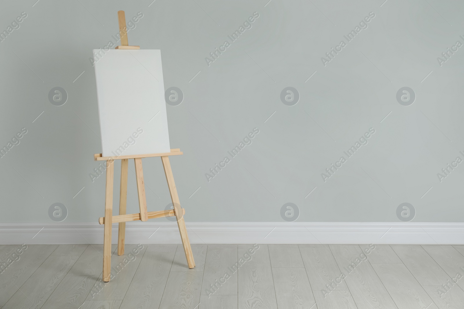 Photo of Wooden easel with blank canvas near light wall. Space for text