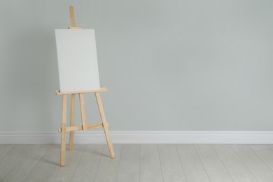 Wooden easel with blank canvas near light wall. Space for text