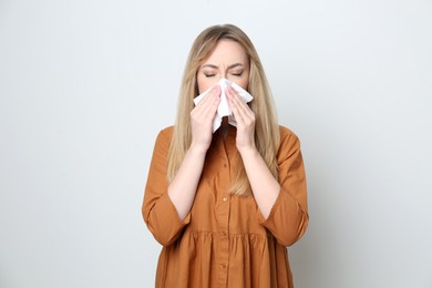 Young woman with tissue suffering from runny nose on white background