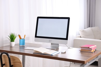 Stylish workplace with computer, books and houseplant on wooden table in room