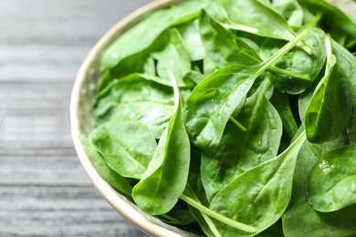 Bowl of fresh green healthy spinach on dark wooden table, closeup