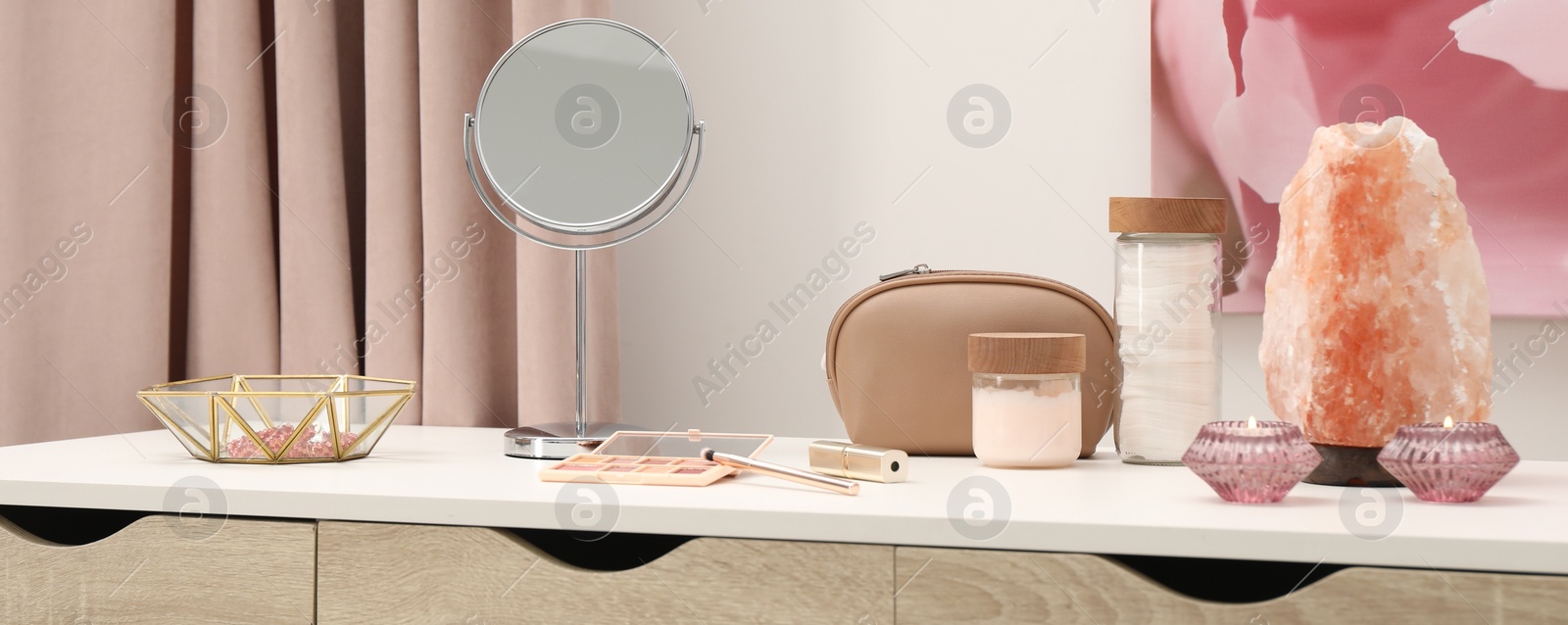 Image of Makeup room. Mirror, cosmetic products, jewelry and burning candles on dressing table indoors, banner design