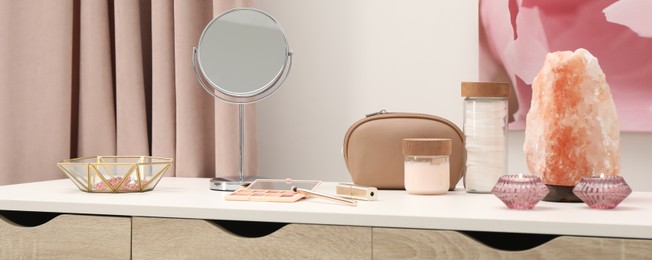 Makeup room. Mirror, cosmetic products, jewelry and burning candles on dressing table indoors, banner design