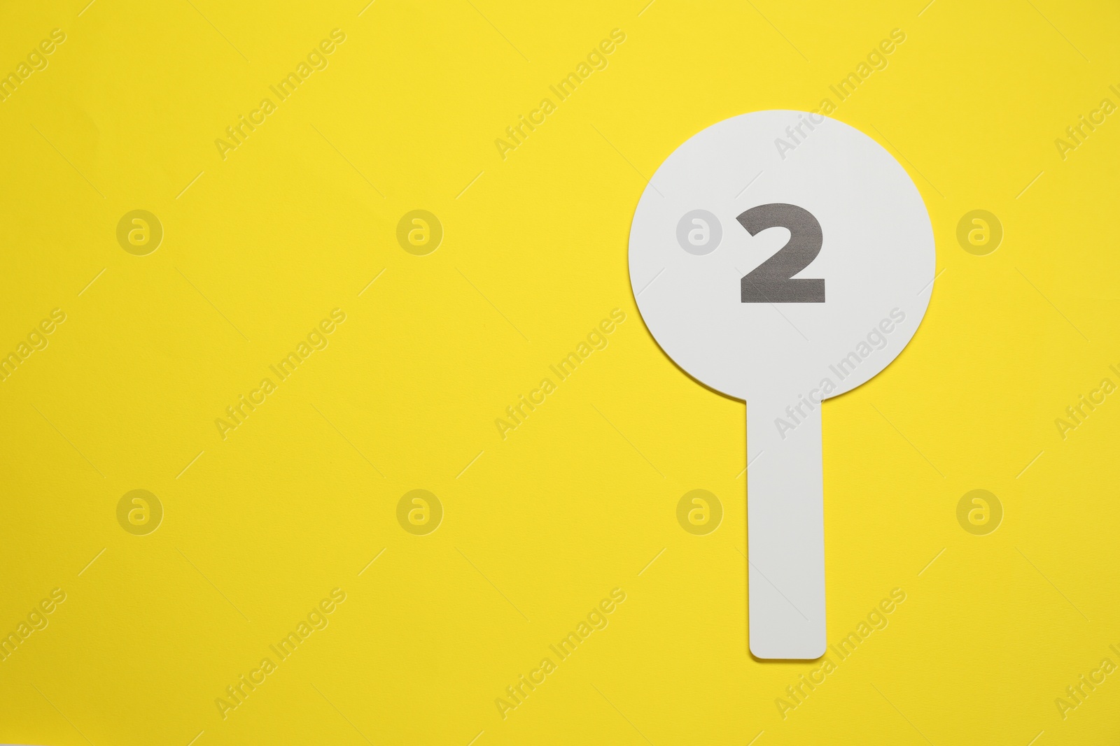 Photo of Auction paddle with number 2 on yellow background, top view. Space for text