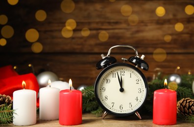 Photo of Alarm clock, burning candles and Christmas decor on wooden table, bokeh effect