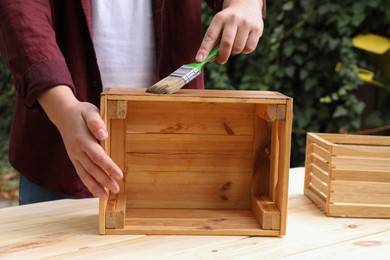 Man applying wood stain onto crate at table outdoors, closeup