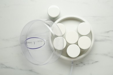 Modern yogurt maker with jars on white marble table, flat lay