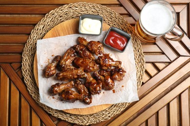 Photo of Tasty chicken wings, mug of beer and sauces on wooden table, flat lay. Delicious snack