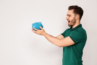 Young man with piggy bank on light background