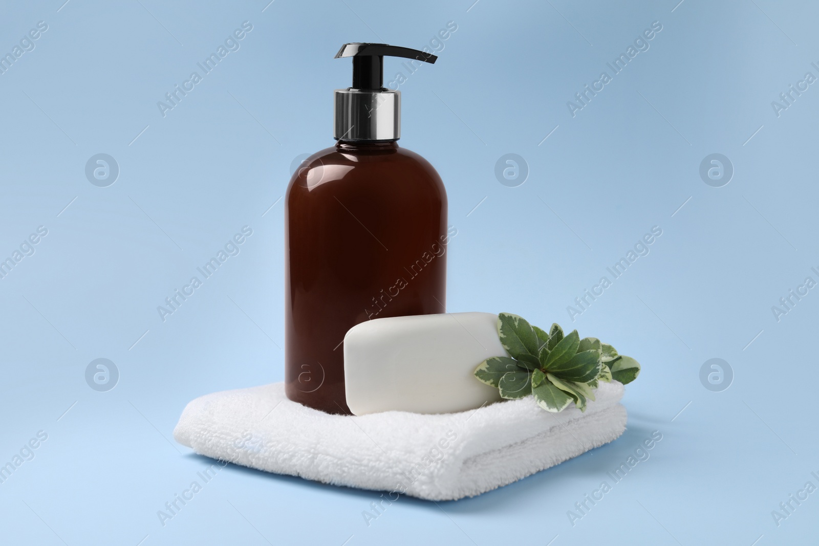 Photo of Soap bar, bottle dispenser and towel on light blue background
