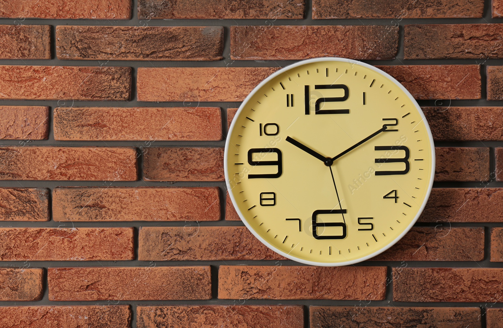 Photo of Stylish analog clock hanging on brick wall. Space for text