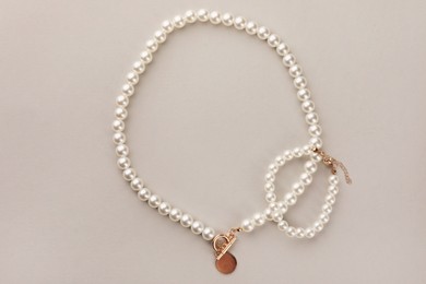 Elegant pearl necklace and bracelet on beige background, top view