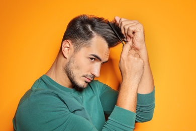 Photo of Young man with comb posing on color background. Trendy hairstyle