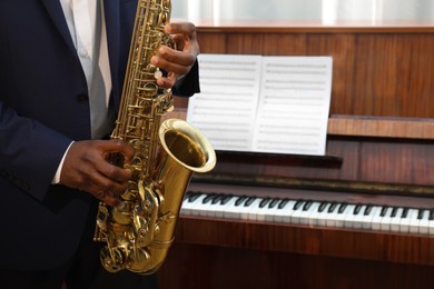 Photo of African-American man playing saxophone indoors, closeup with space for text. Talented musician