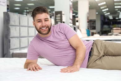 Photo of Smiling man lying on orthopedic mattress in store