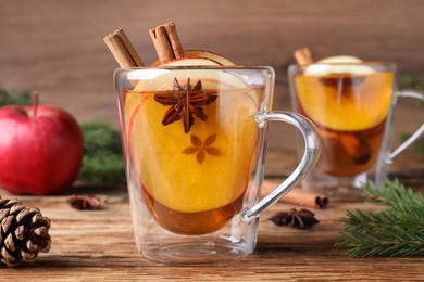 Photo of Hot mulled cider and fir branches on wooden table, closeup