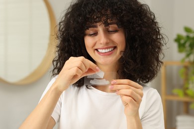 Photo of Young woman holding teeth whitening strips in bathroom