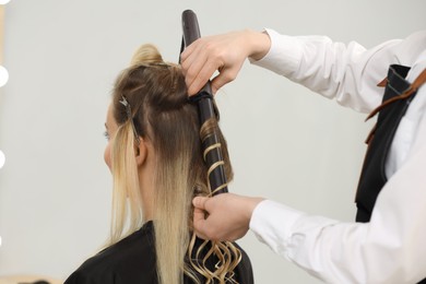 Photo of Hair styling. Hairdresser curling woman's hair in salon, closeup