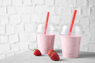 Tasty milk shake in plastic cups and strawberries on white table