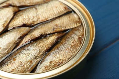 Open tin can of sprats on blue wooden table, closeup