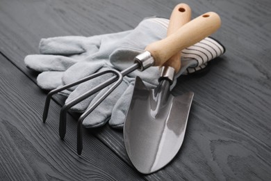 Photo of Gardening gloves, trowel and rake on grey wooden table, closeup