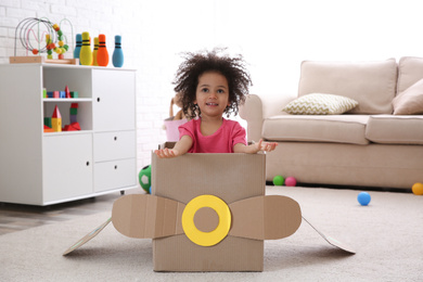 Photo of Cute African American child playing with cardboard plane at home