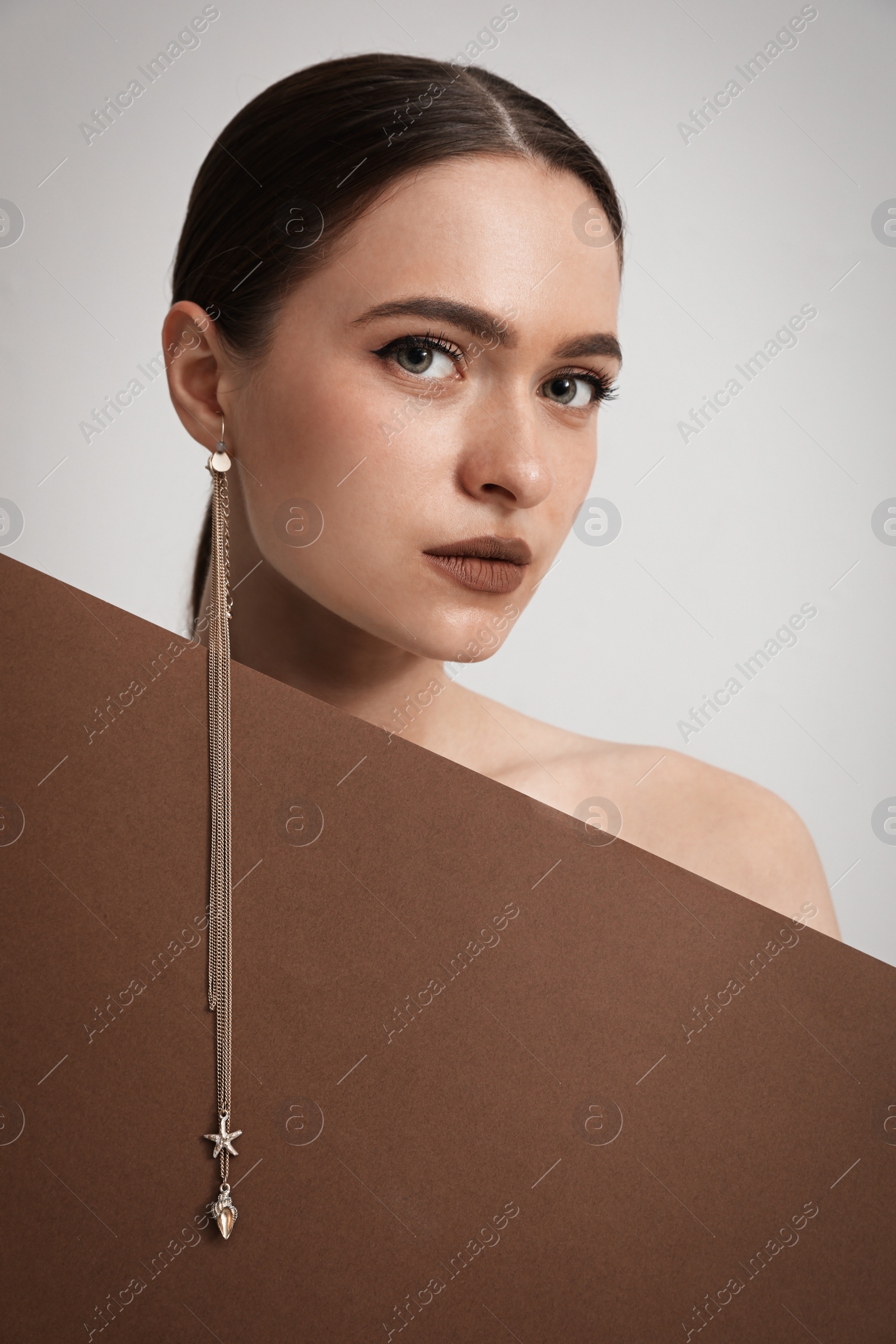 Photo of Beautiful young woman with stylish earring posing on light background