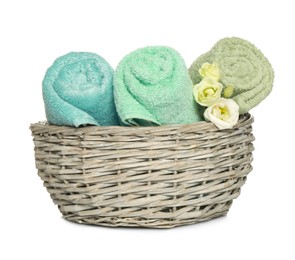 Photo of Wicker basket with rolled soft terry towels and flowers on white background