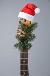 Photo of Guitar with Santa hat and fir tree branch on grey background. Christmas music